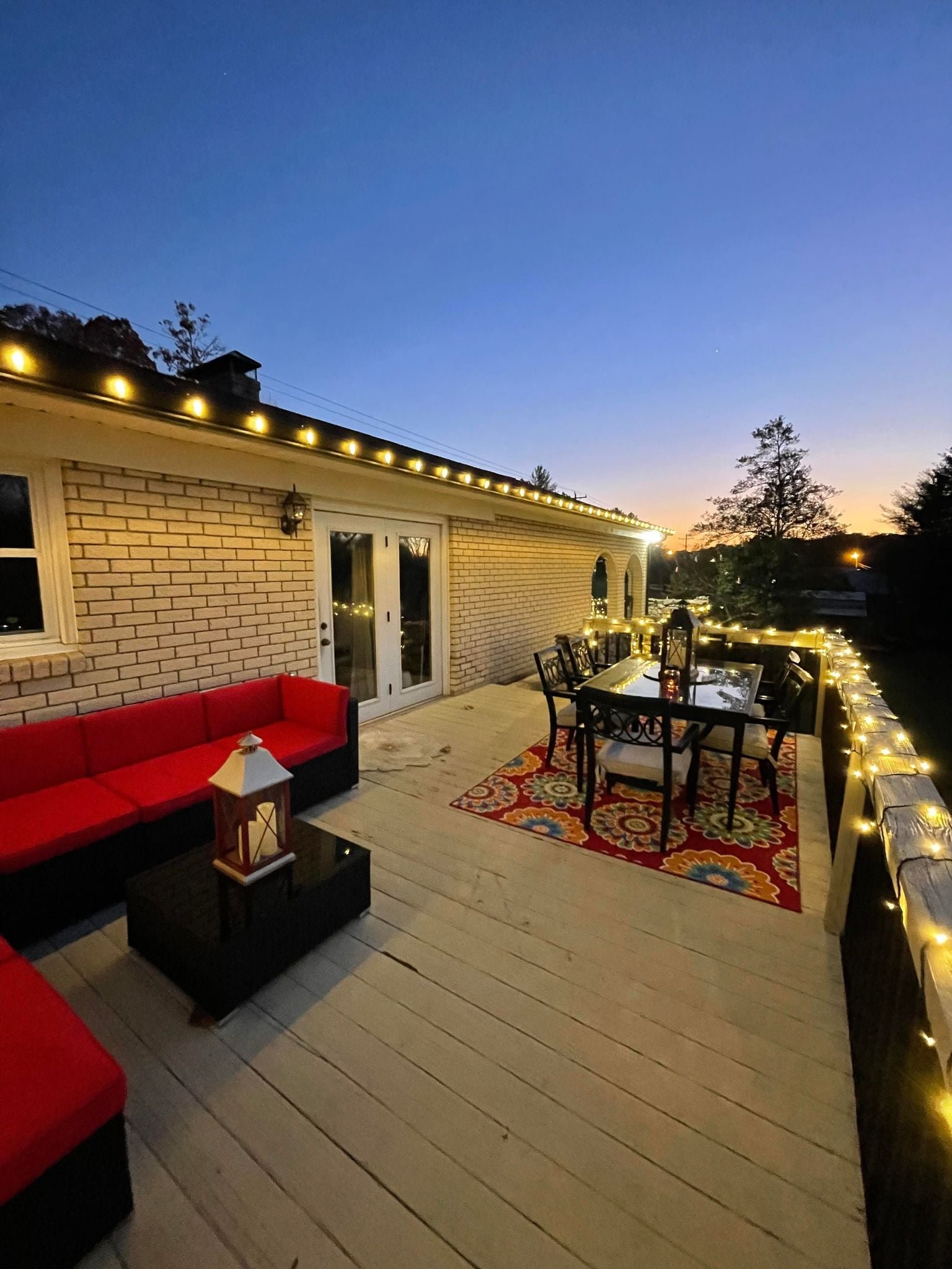 Warm white string lights along a roofline and backyard deck at dusk