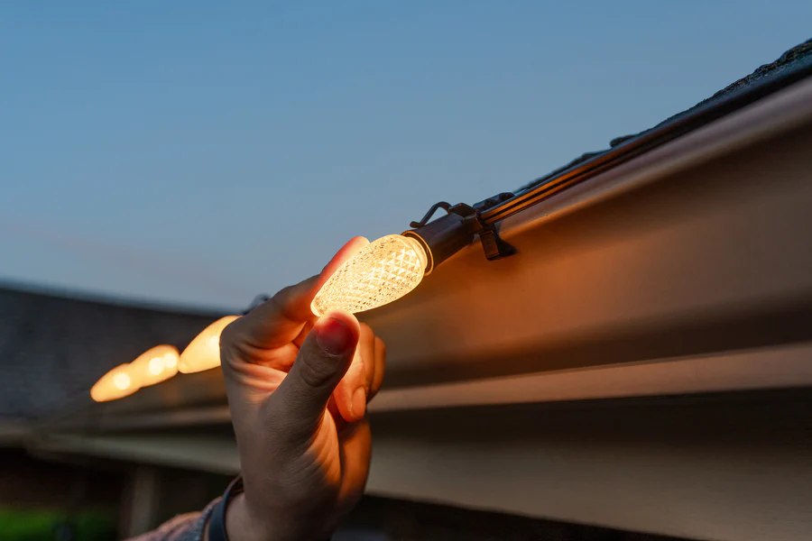 Technician clipping a warm white LED holiday light to a gutter