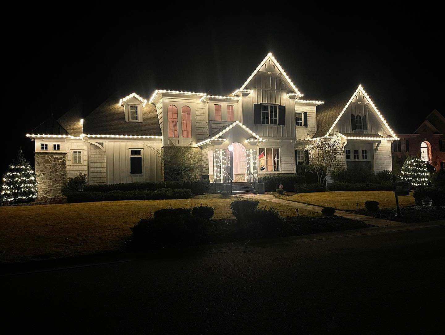 Two-story home outlined with warm white roofline Christmas lights at night