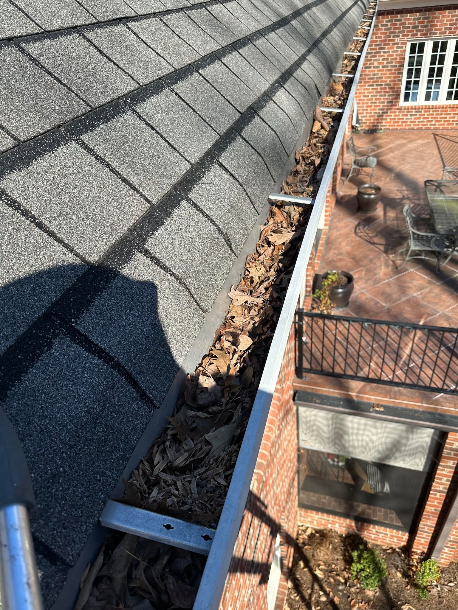 Leaf-filled gutter on a brick home with a gutter cleaning tool