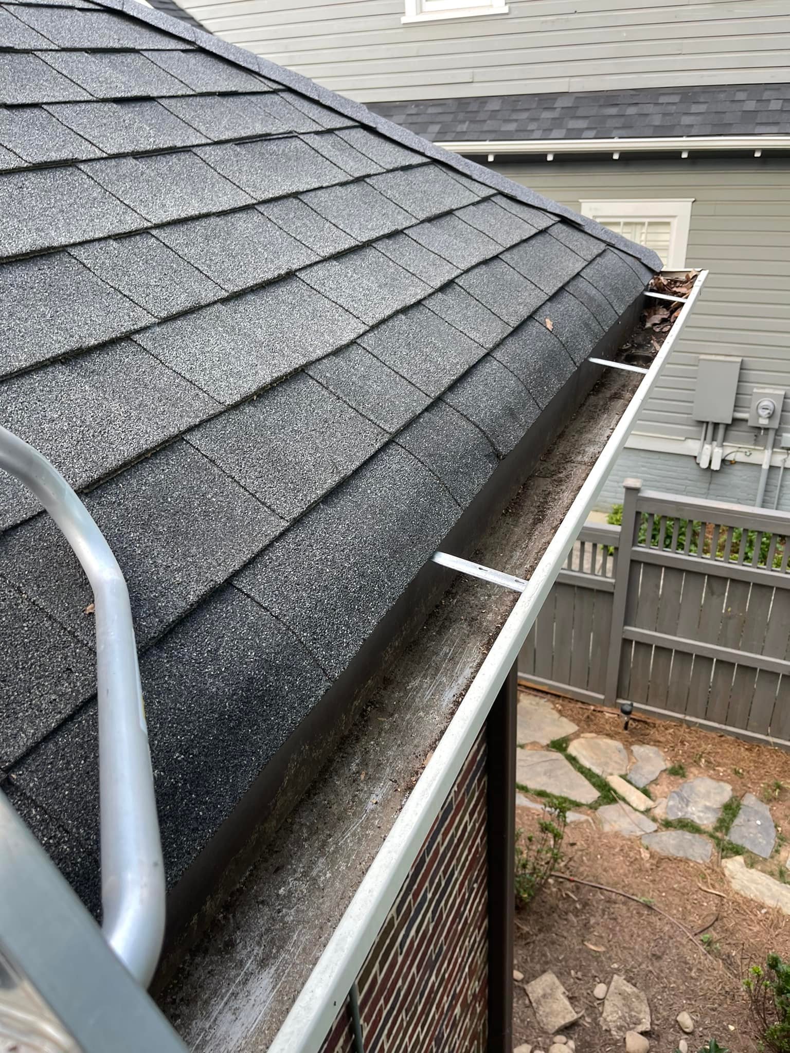 Gutter on a shingle roof with debris and a cleaning tool